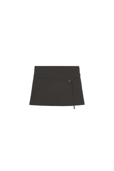 Front view of a black miniskirt with a thin belt detail and buckle at the waist.