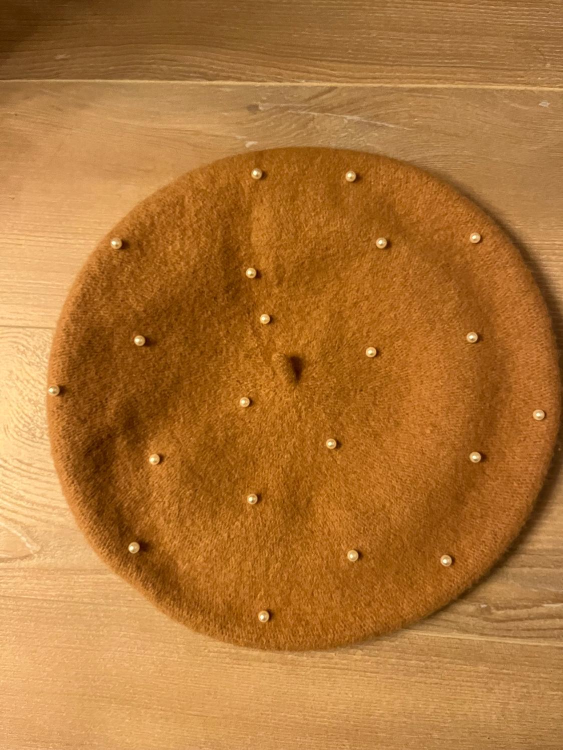Brown beret with small decorative pearls on a light wooden surface.