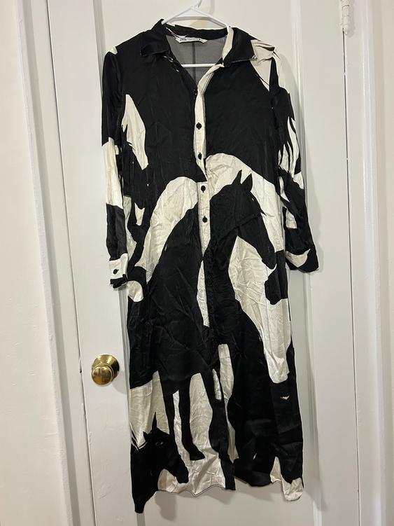 Long dress hanging on a door, with a black and white horse print, front buttons, and a classic collar.