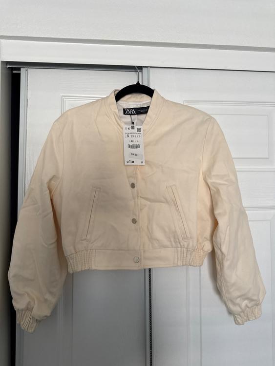 Beige jacket hanging on a hanger in front of a white door. Visible tag with price of $59.90 and size S.