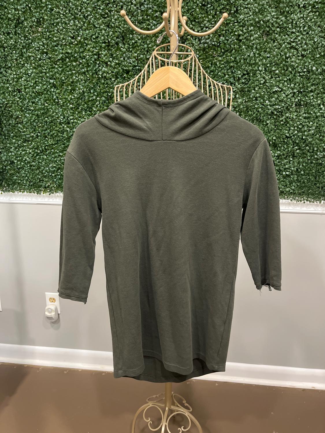 Olive green hoodie with three-quarter sleeves on a metal hanger, wall background with artificial plants.