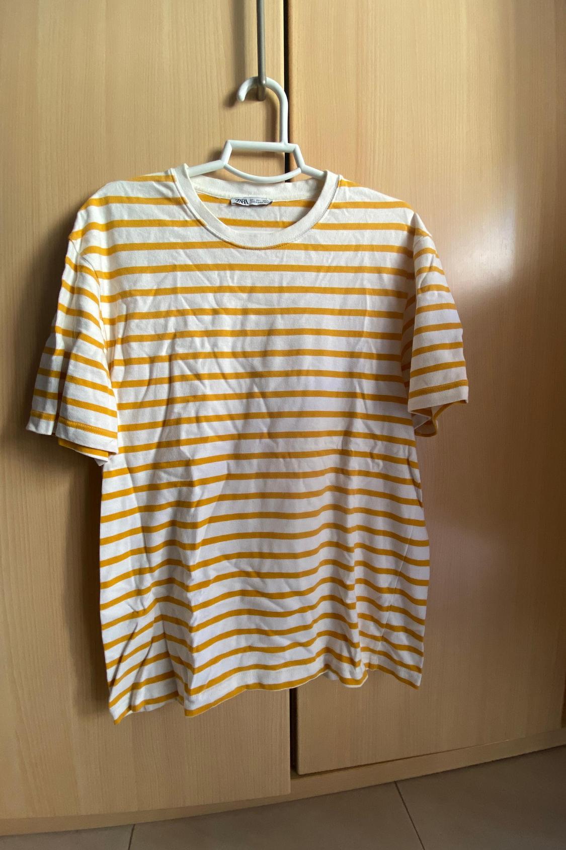 Front view of a yellow and white striped t-shirt hanging on a hanger.