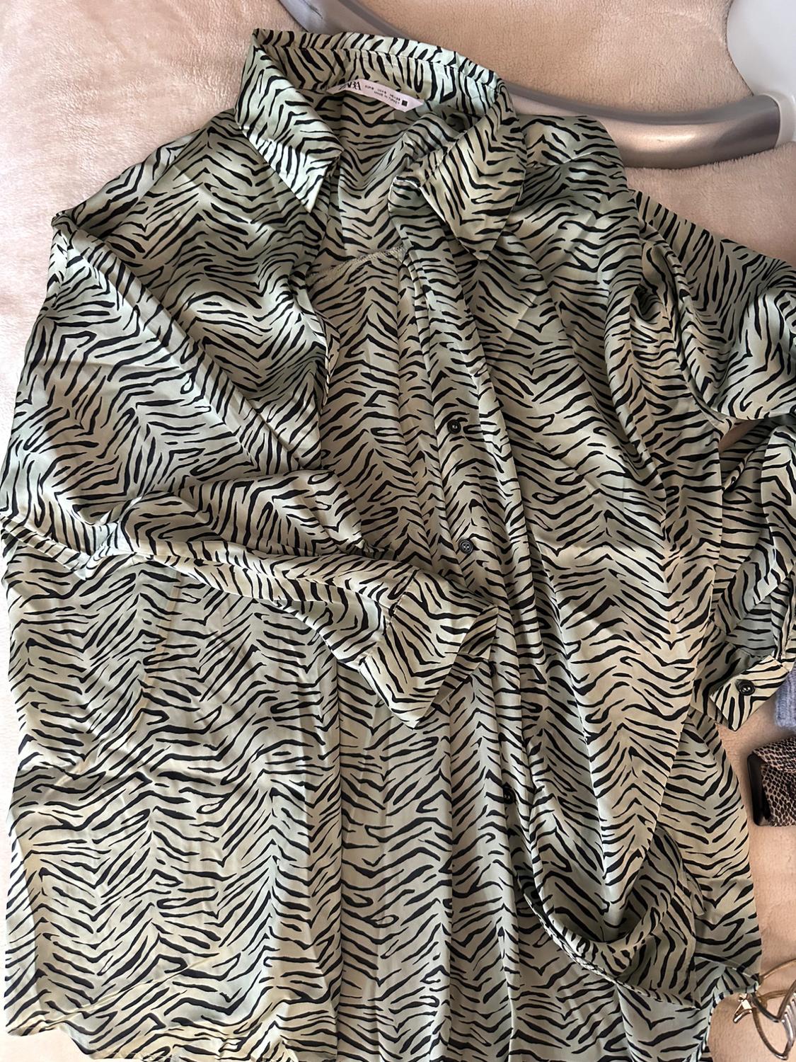 Satin shirt with a zebra print in beige and black tones, placed on a light surface, with a silver hanger.