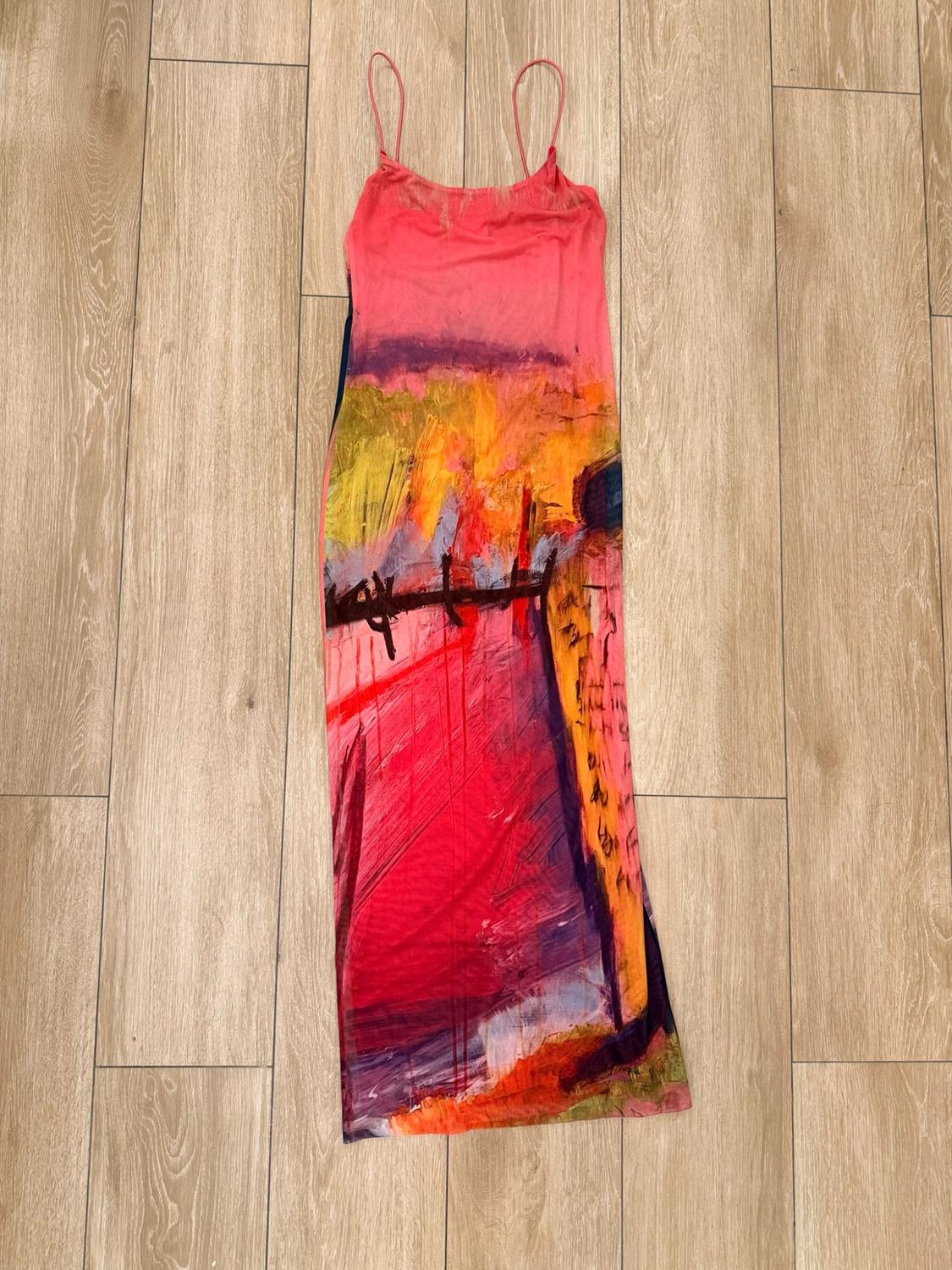 Maxi dress with spaghetti straps and an abstract, paint-style print in shades of pink, red and yellow, on a wooden floor.