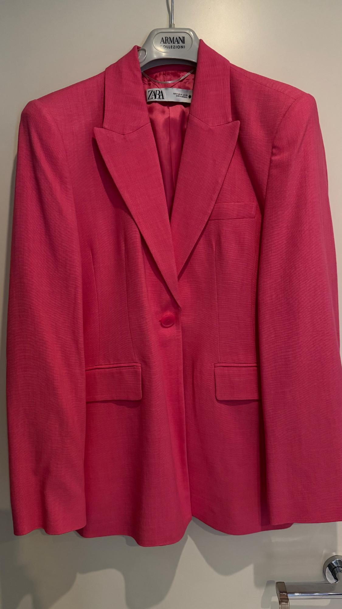 Pink blazer hanging on a hanger. Visible text: ARMANI COLLEZIONI, ZARA, MADE IN MOROCCO.
