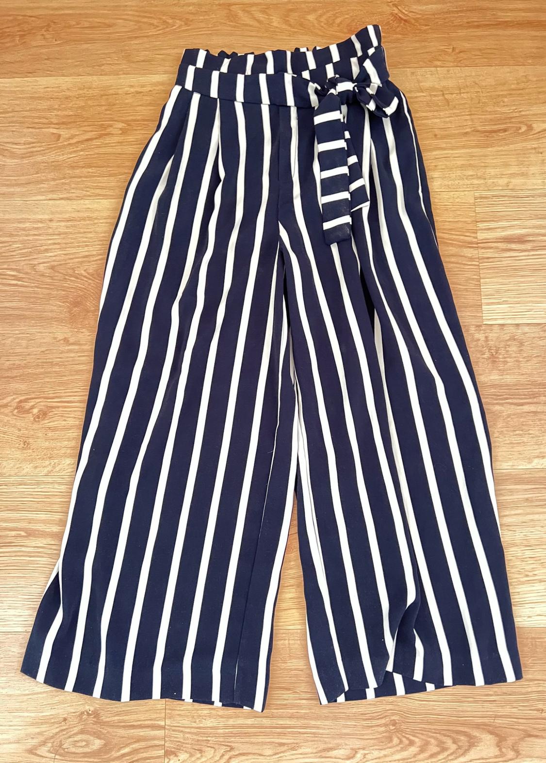 Navy blue and white vertical-striped wide-leg trousers with a high-waisted gathered waist and tie belt, on a wooden floor.