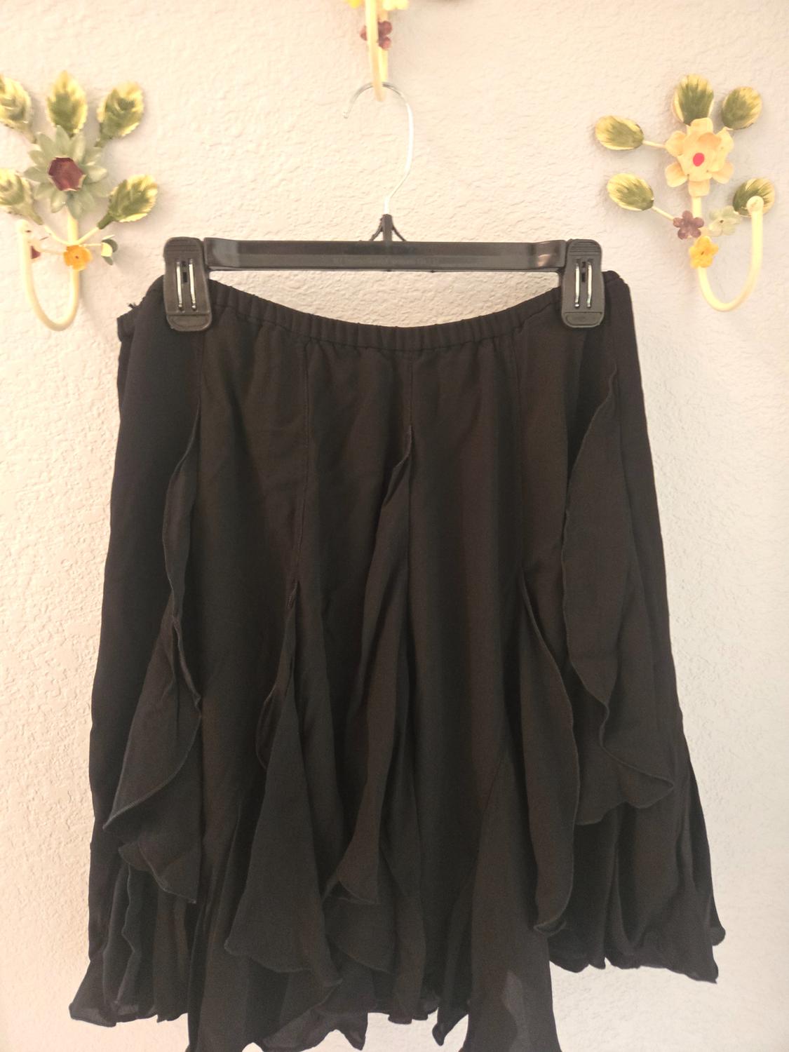 Black ruffled skirt hanging on a black hanger on a white wall decorated with ceramic flowers.