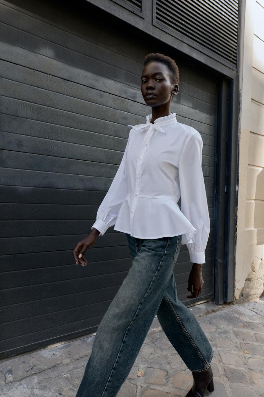 White peplum shirt set with bow, round neck, long sleeves, and button closure, paired with blue jeans.