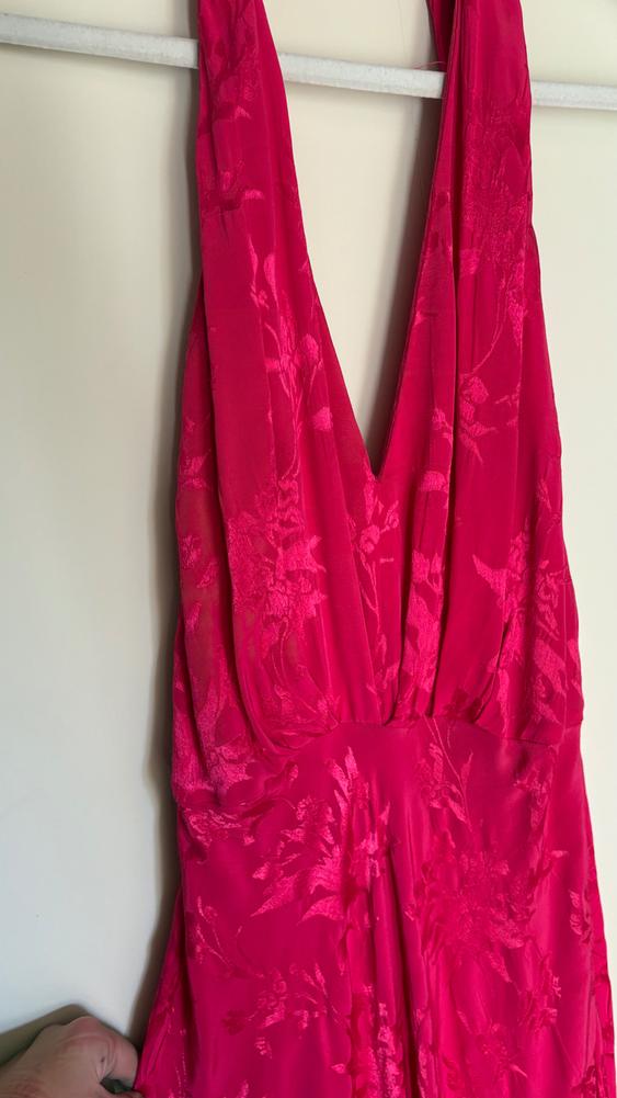 A red dress with a V-neck and floral print is hanging on a white hanger, while a hand holds the bottom of the dress.