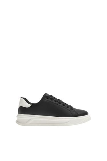 Side view of a black trainer with a white sole and white detailing on the heel.