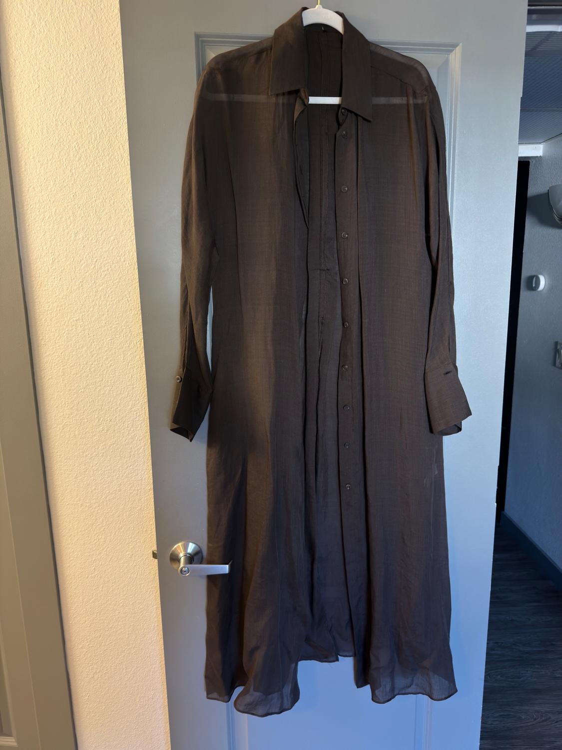 Dark brown semi-sheer long shirt hanging on a grey door. Relaxed indoor setting.