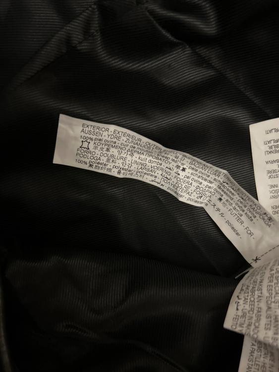 Etiqueta de composición en tela negra, texto en varios idiomas: "OUTER: 100% sheepskin. LINING: 100% polyester".