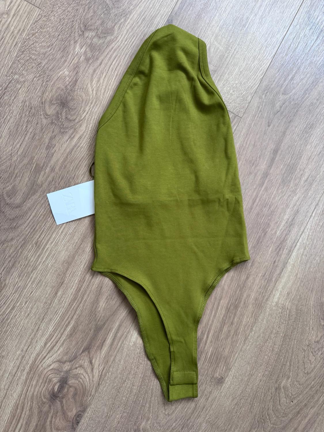 Olive-green ribbed bodysuit on a wooden floor. White label with the text ZARA.
