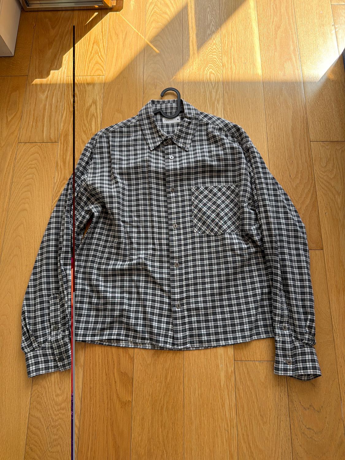 Black and white plaid shirt hanging on a hanger over a wooden floor illuminated by sunlight.