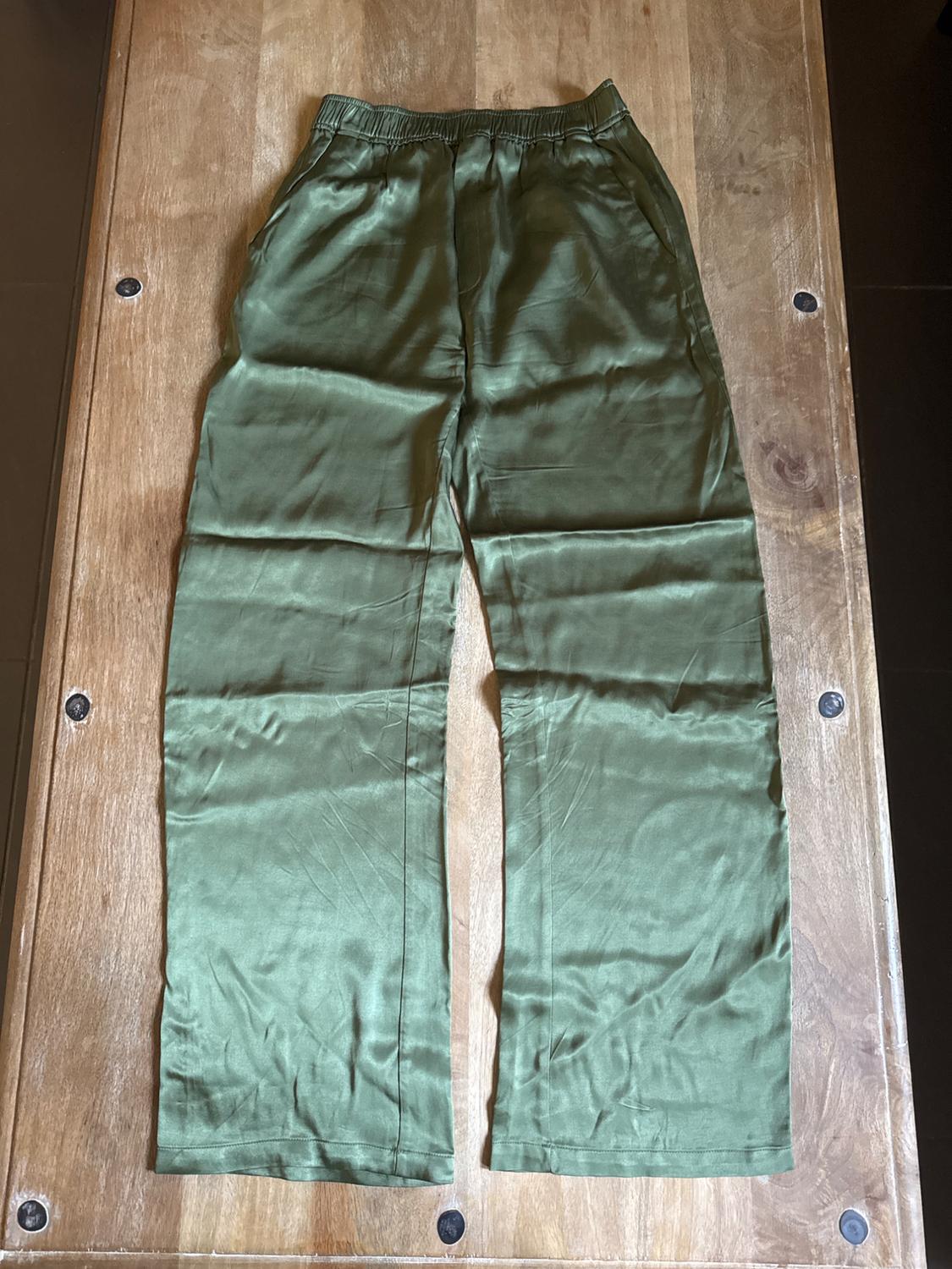 Green satin fabric trousers with an elasticated waistband, placed on a wooden table.