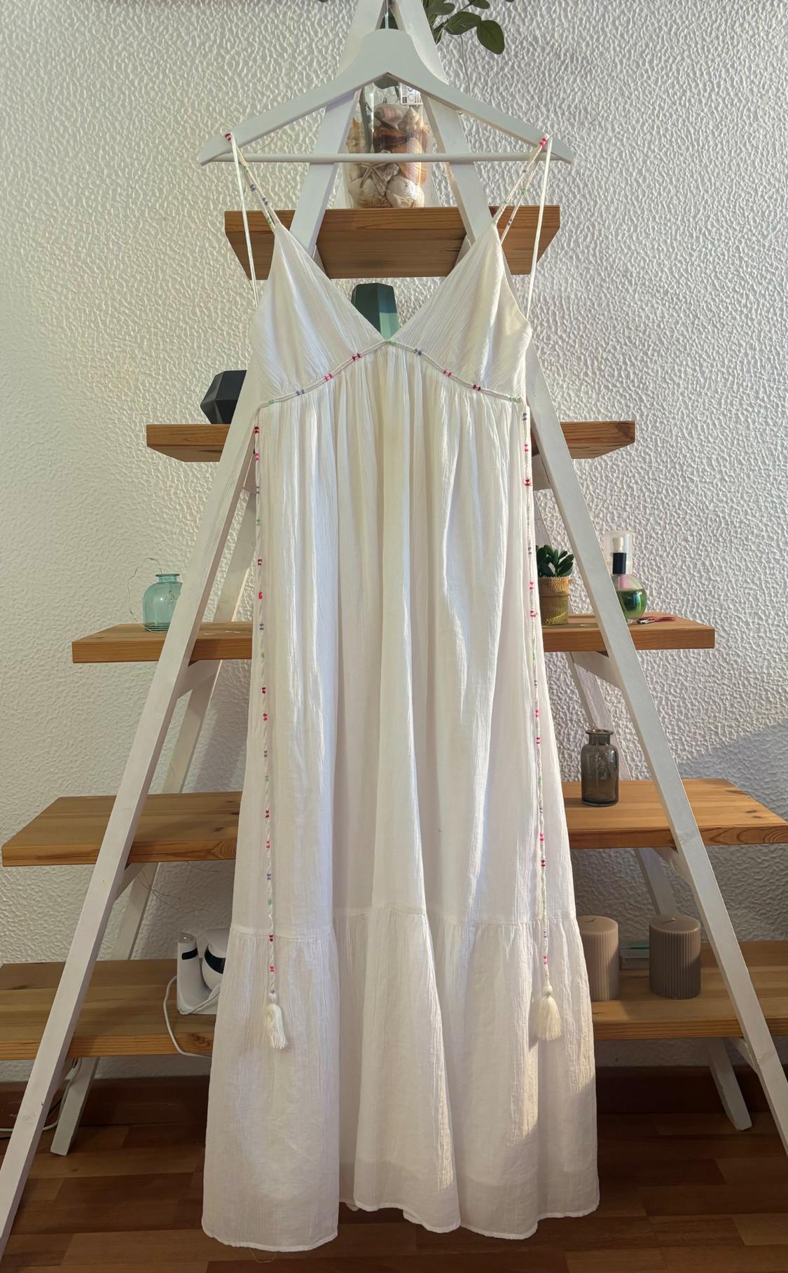 White dress hanging on a wooden ladder with shelves. Textured wall backdrop and decorative objects on the shelves.