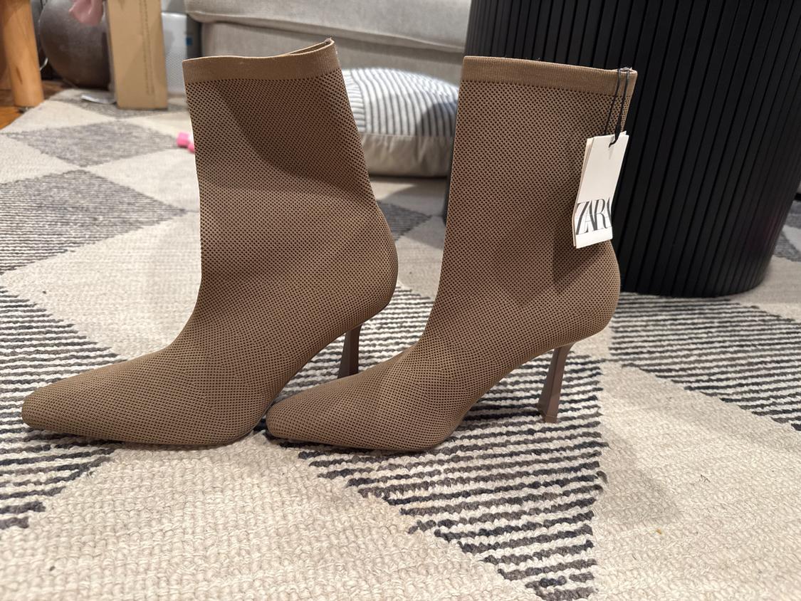 Brown heeled ankle boots with mesh texture on a checked rug. Visible label with text "ZARA". Background with furniture.