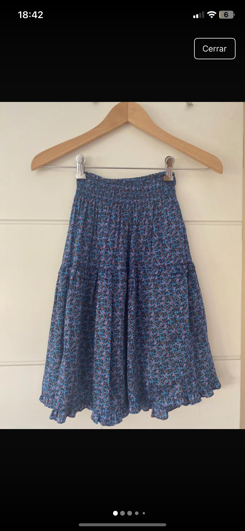 Blue skirt with a floral print in shades of pink and lilac, hanging on a wooden coat hanger against a white background. Visible text: "Close".