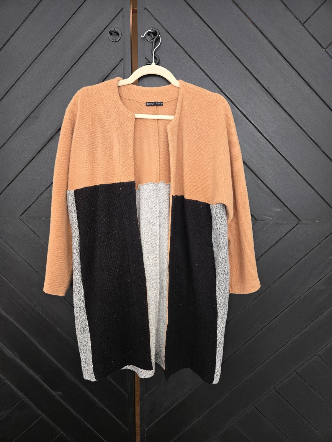 Front view of a tricolor coat in camel, black, and gray tones, with an open design and long sleeves.