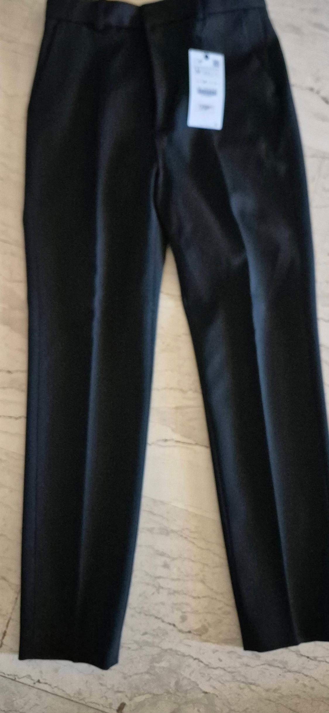 Black trousers on a light marble background, with a white label visible at the top.