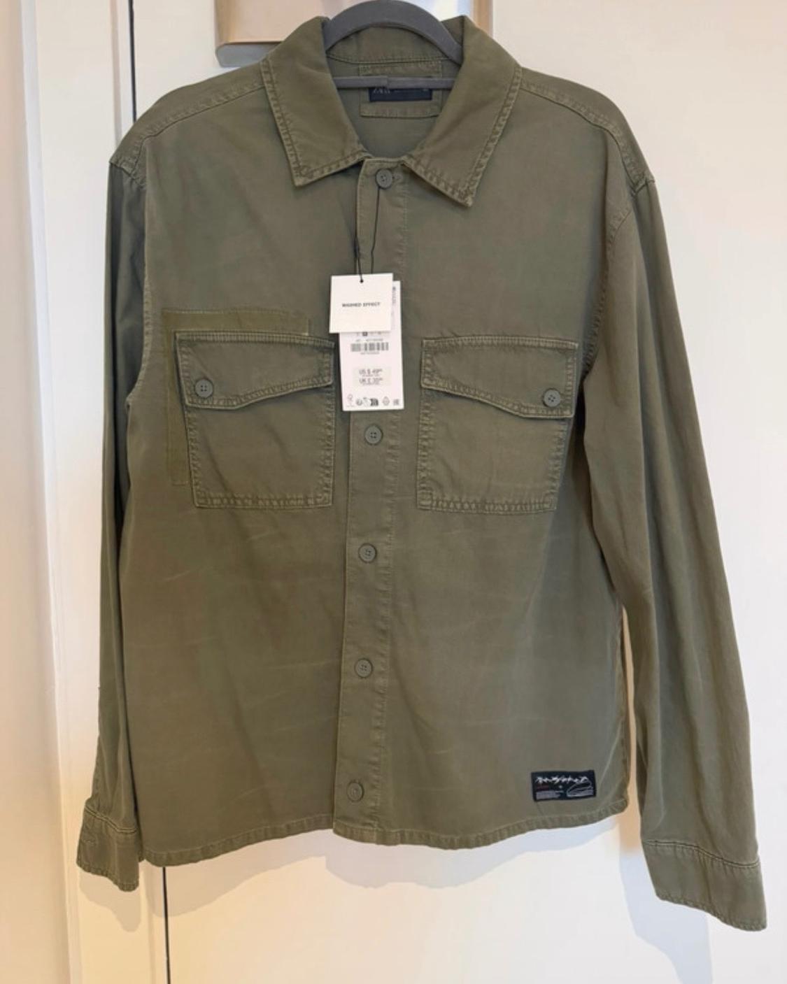 Olive green overshirt on a hanger. Long sleeves, button fastening, chest pockets and a hang tag with the text WASHED EFFECT.