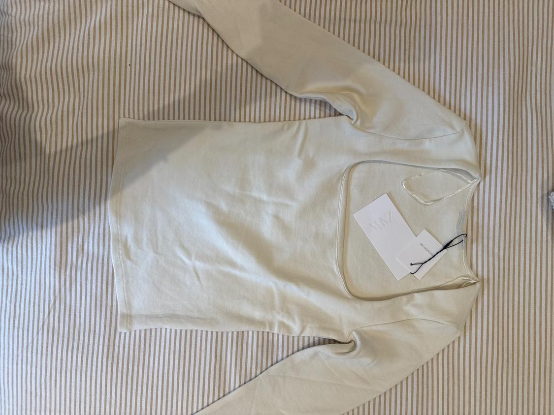 Cream long-sleeved top with a wide neckline on a striped background. Casual style. Label with ZARA text.