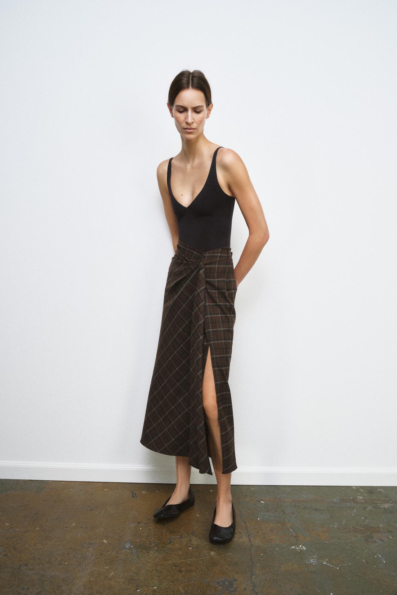 Black strappy bodysuit and long brown skirt set with a side slit and plaid print.