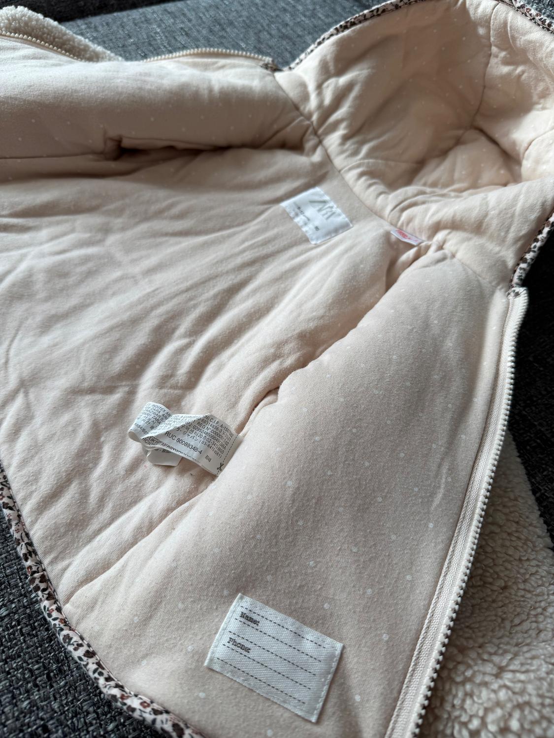 Beige padded jacket open on a grey sofa, with visible tags and leopard print trim.