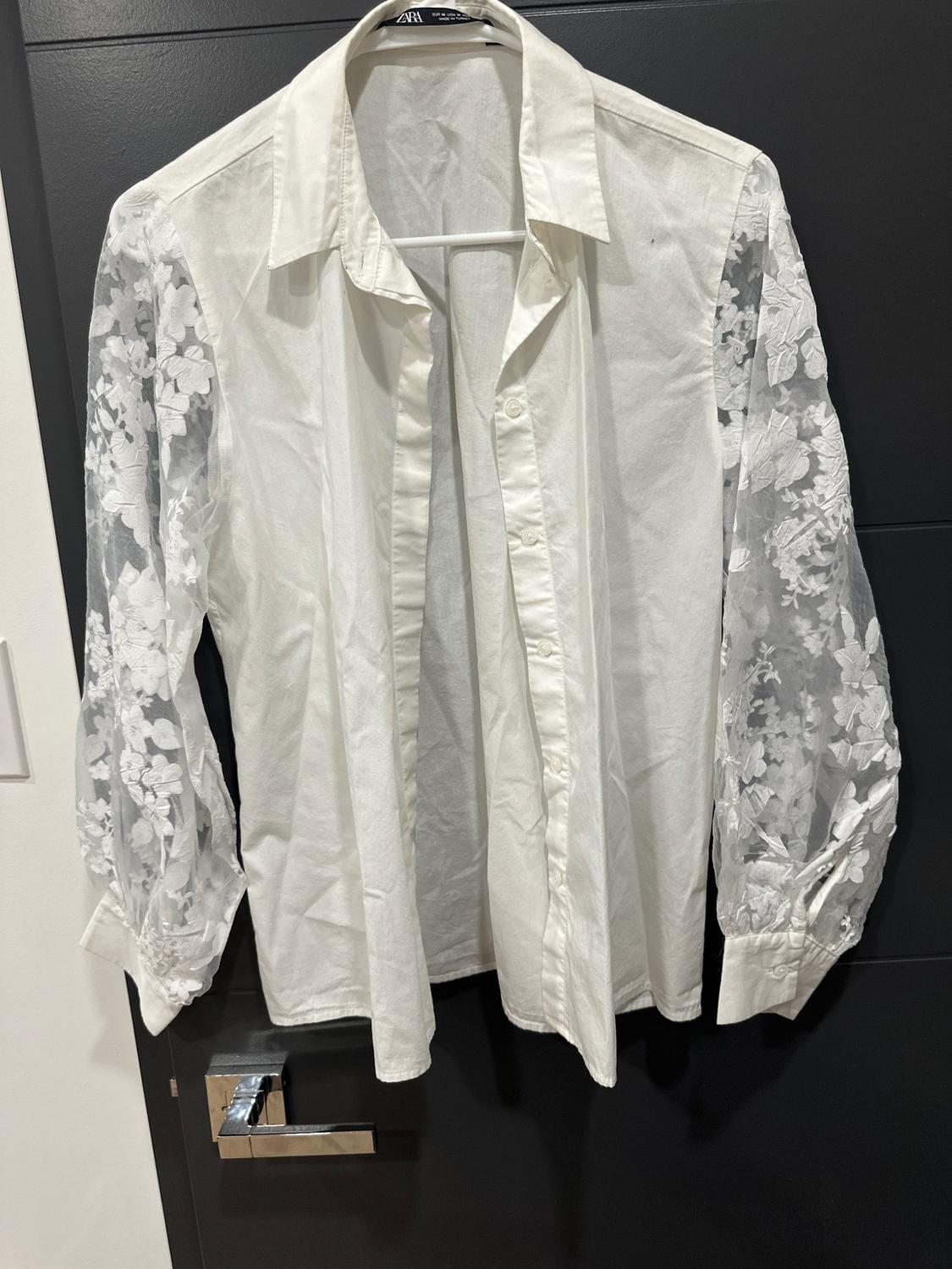 White shirt hanging on a black door, with sheer floral lace sleeves.