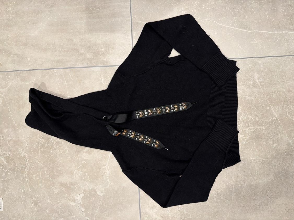 Black hoodie with decorative drawstrings on a grey tiled floor.