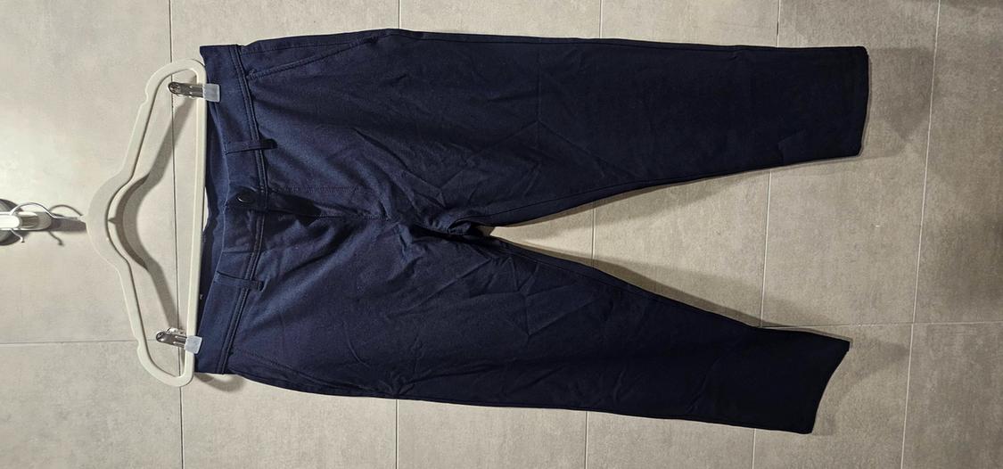 Navy blue trousers clipped to a white hanger, laid out on a light tiled floor.