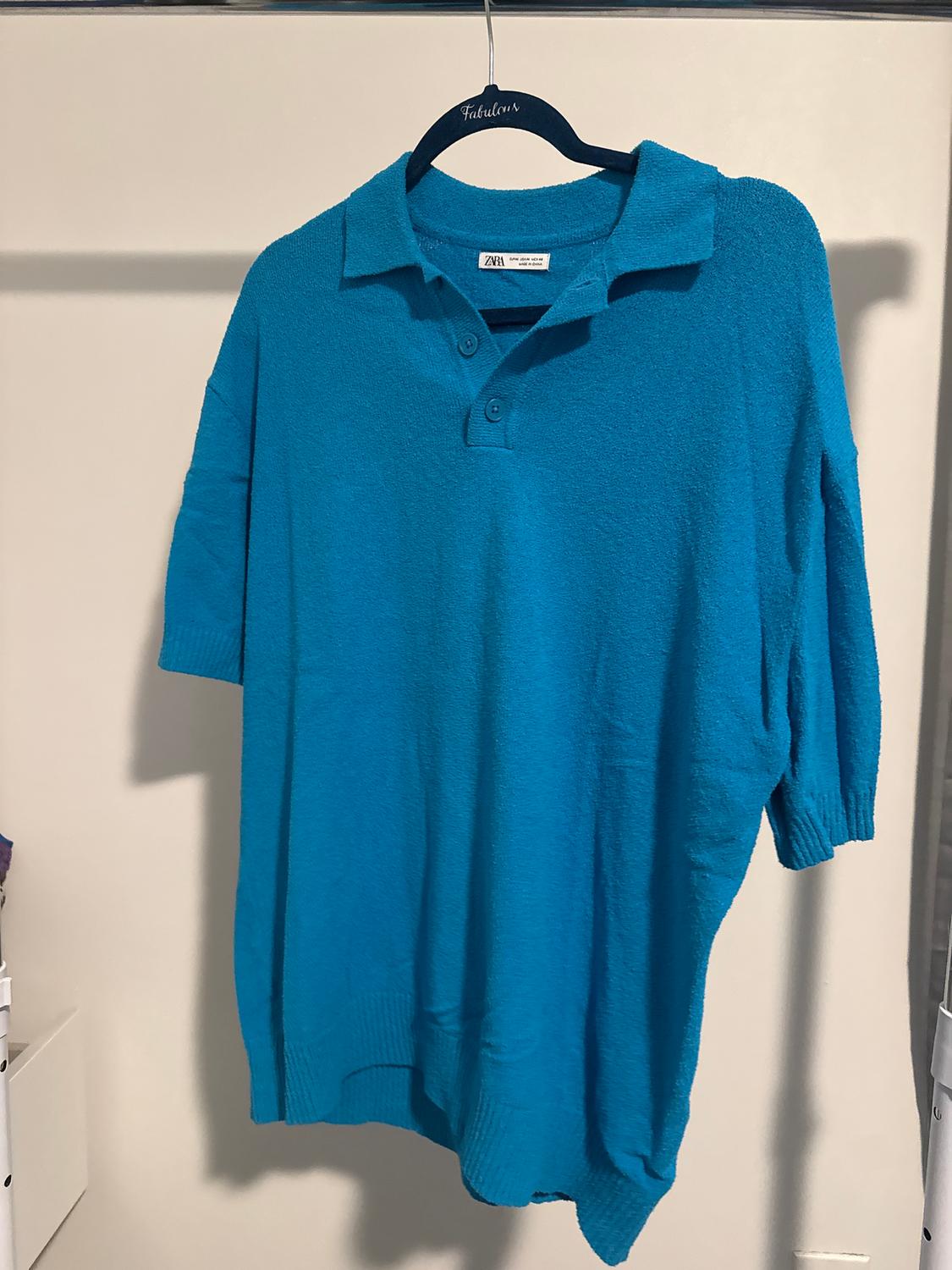 Blue polo neck jumper with buttons hanging on a black hanger with the word "Fabulous", against a white background.