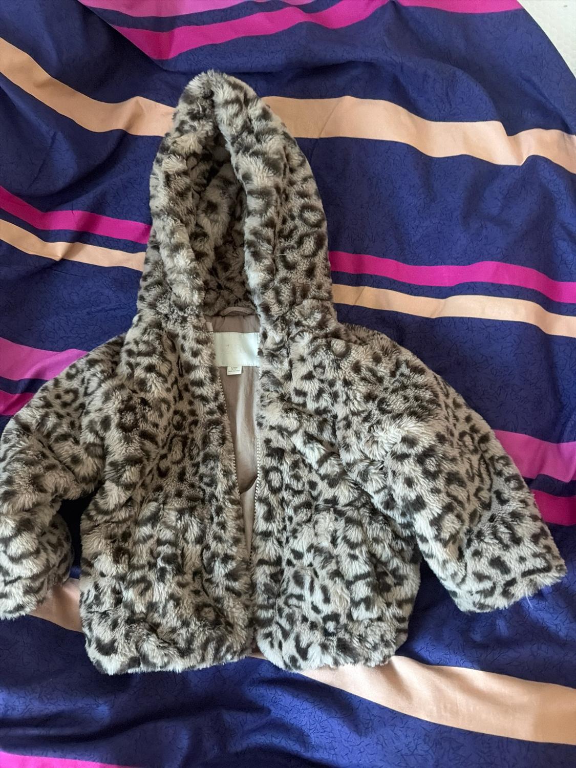 Leopard-print faux fur hooded jacket, open against a fabric background with blue, pink and beige stripes.