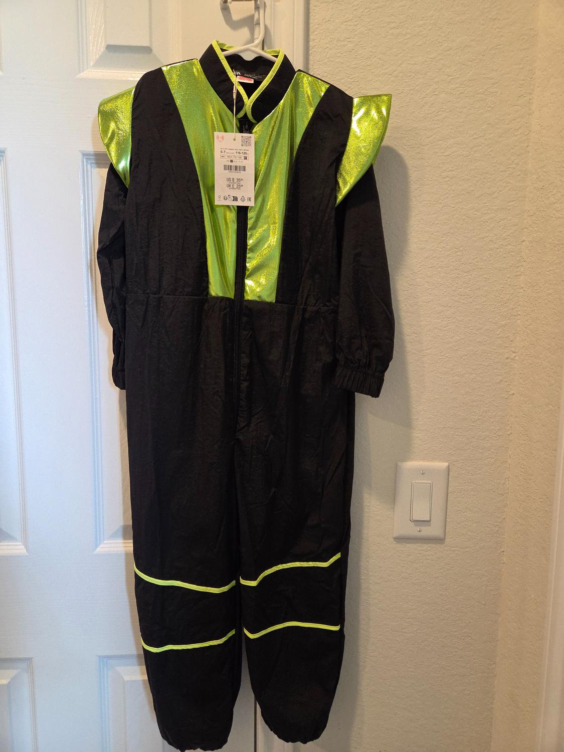 Black jumpsuit with bright green details hanging on a white door. Visible label with sizes US 5-6, UK 4-5.