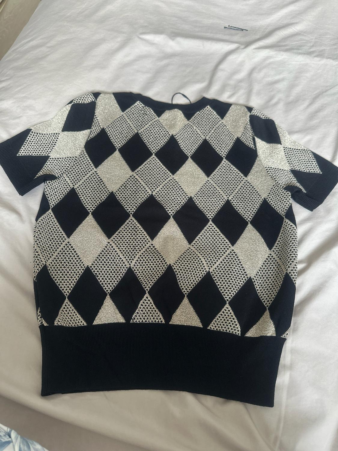 Short-sleeved knitted top with a black and white diamond pattern, laid out on casual, rumpled white bedsheets.