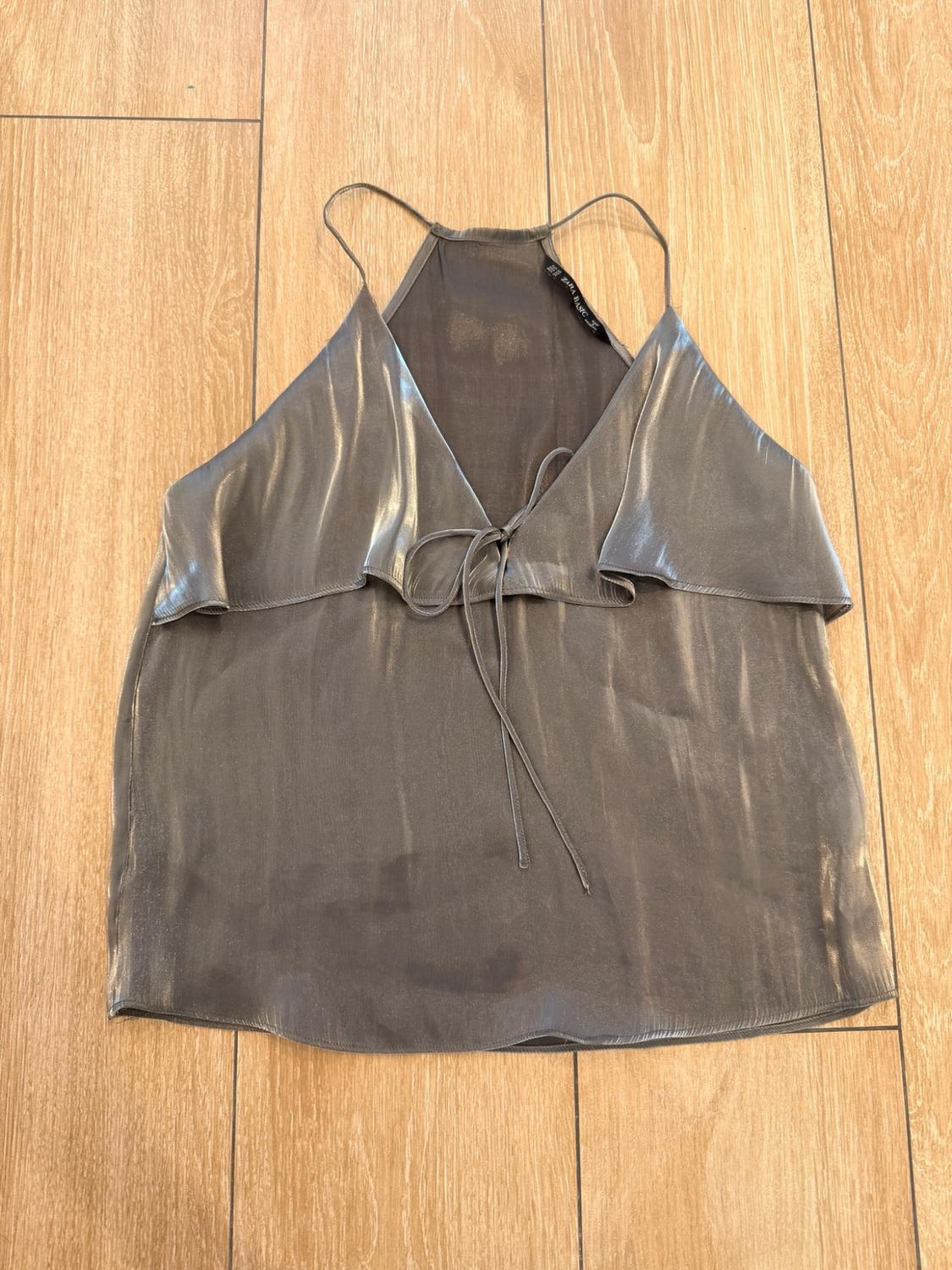 Metallic grey camisole top with V-neckline and front tie detail, on a wooden floor. ZARA BASIC label.
