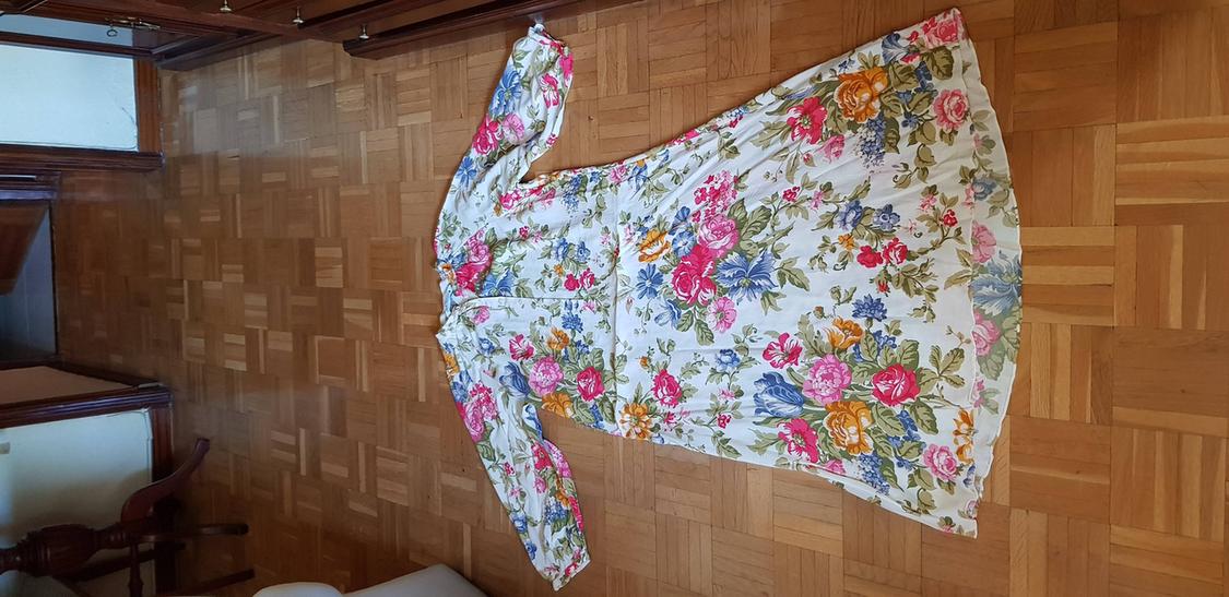 Long-sleeved floral dress on the parquet floor, with a print of pink, blue, and yellow flowers on a white background.