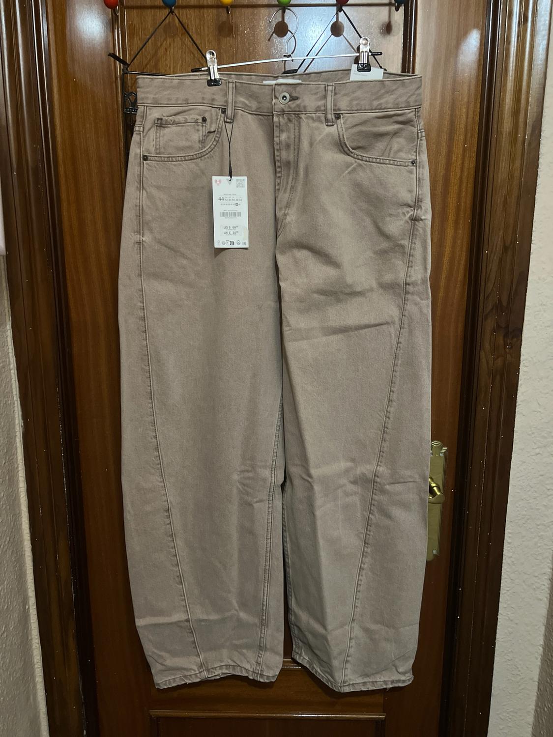 Beige wide-leg trousers with front seams hanging on a wooden door. A label bearing the text 44 can be seen.