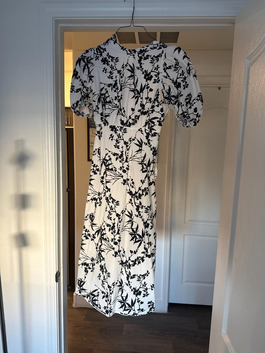 White dress with a black floral print and short puff sleeves, hanging on a hanger in the frame of an open door.