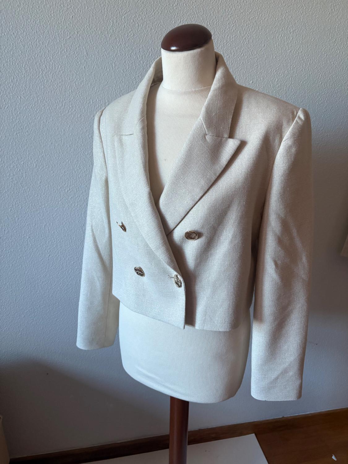 Mannequin in a double-breasted beige jacket with wide lapels, against a white wall background.