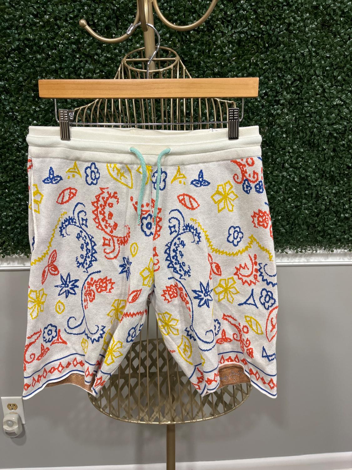 White shorts with a colorful floral and abstract print in red, blue, and yellow, hanging on a gold hanger.