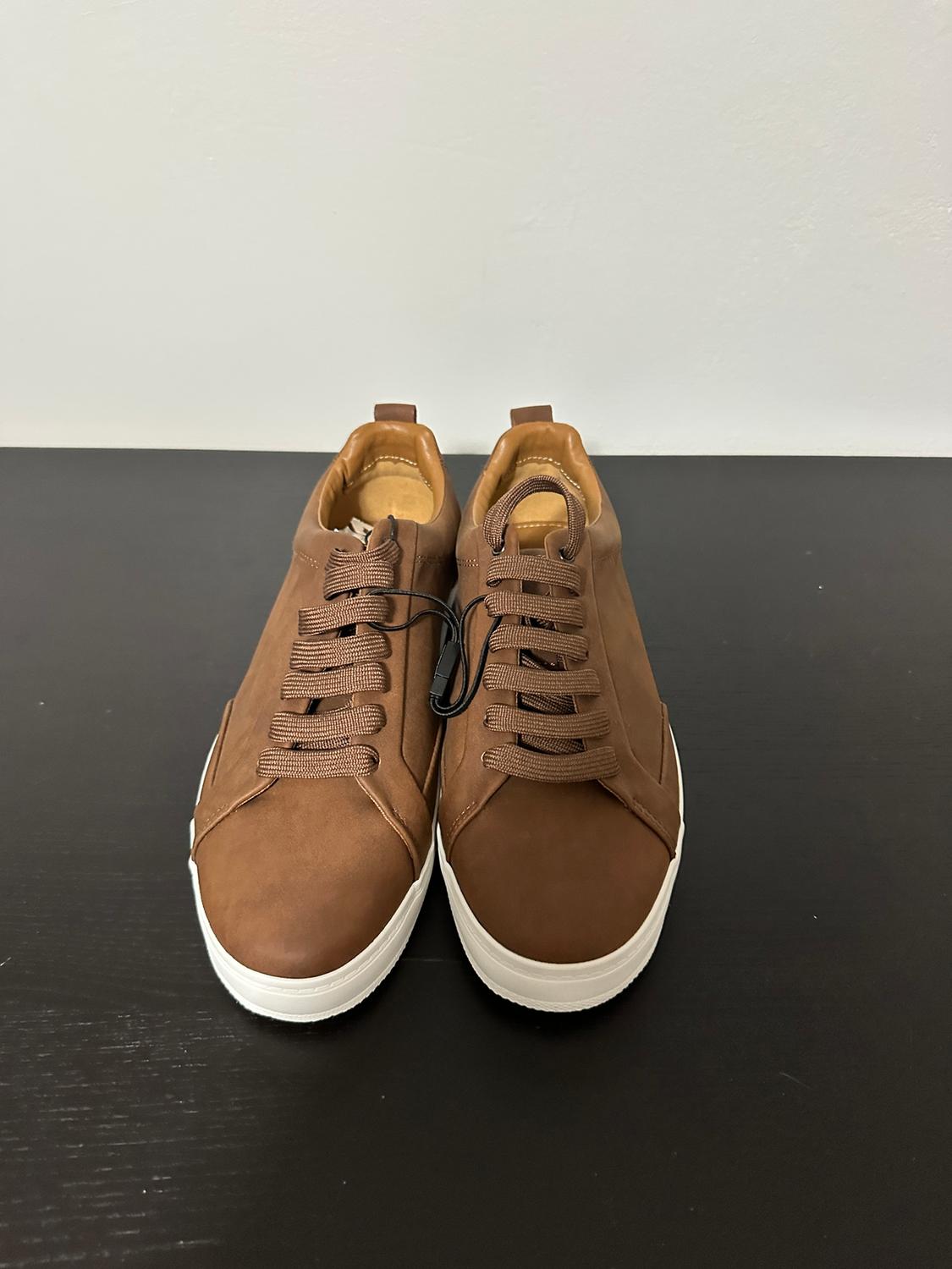Brown lace-up trainers on a black background. White soles contrast with the simple and modern design of the footwear.