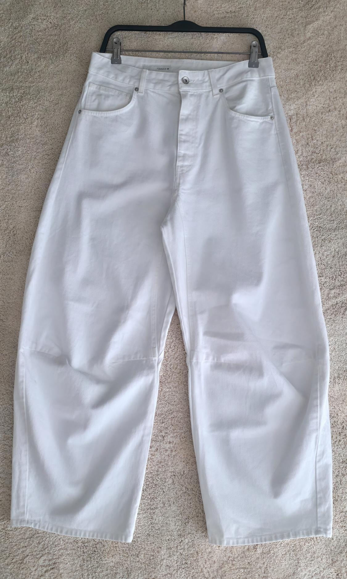 White wide-leg pants with knee seams, hanging from a black hanger over a light-colored rug.