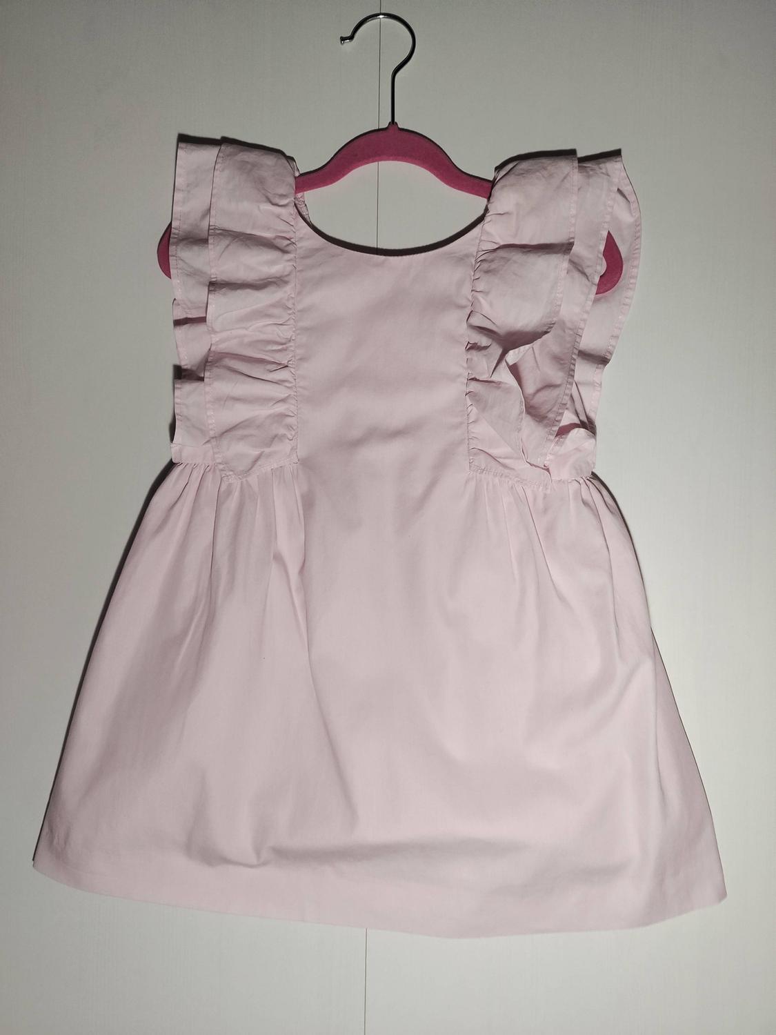 Light pink dress with ruffled shoulders, hanging on a pink hanger against a white background.