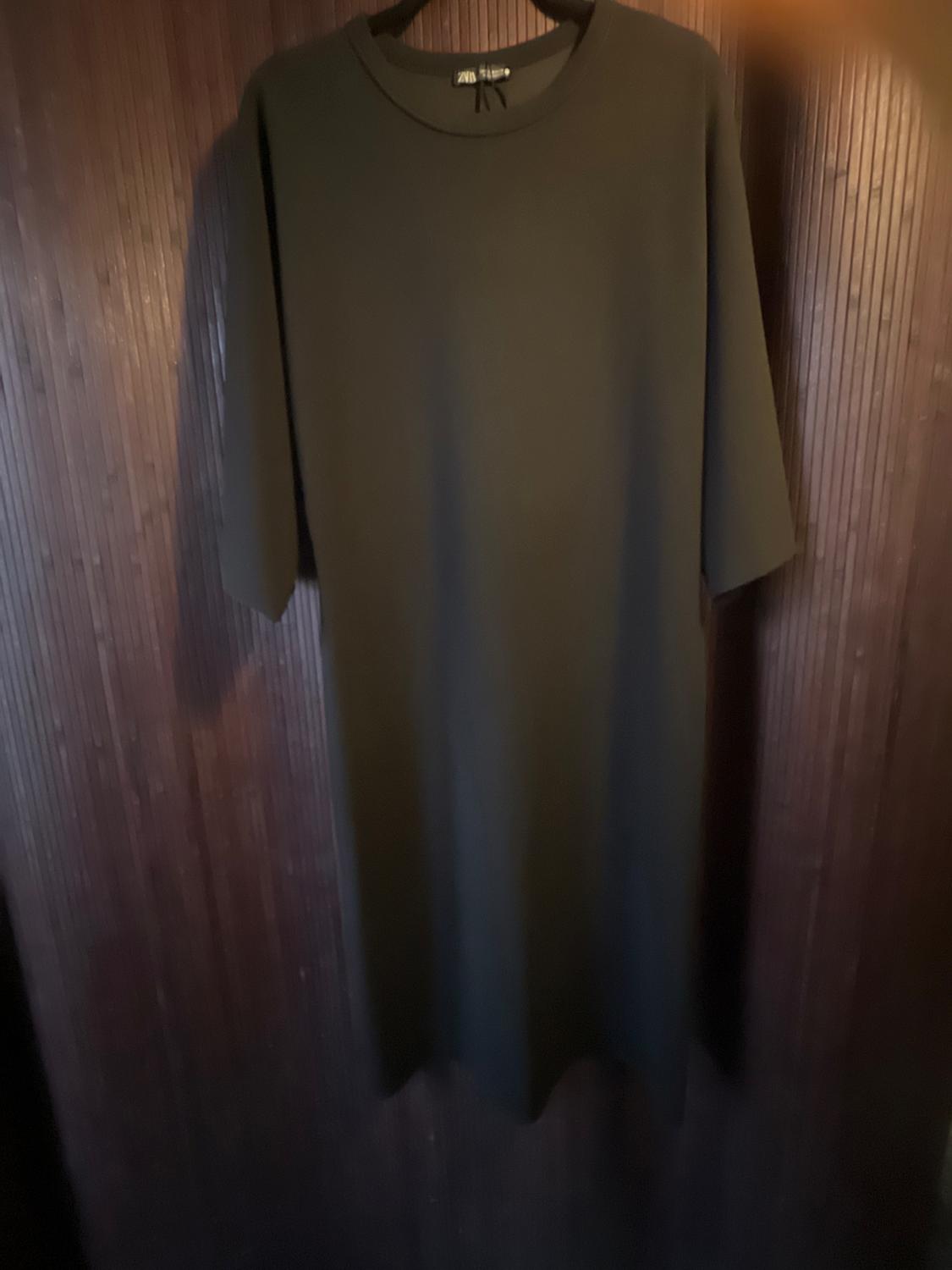 Short-sleeved black dress hanging on a dark wooden wall. The tag says "Zara Basic". Warm and dim atmosphere.