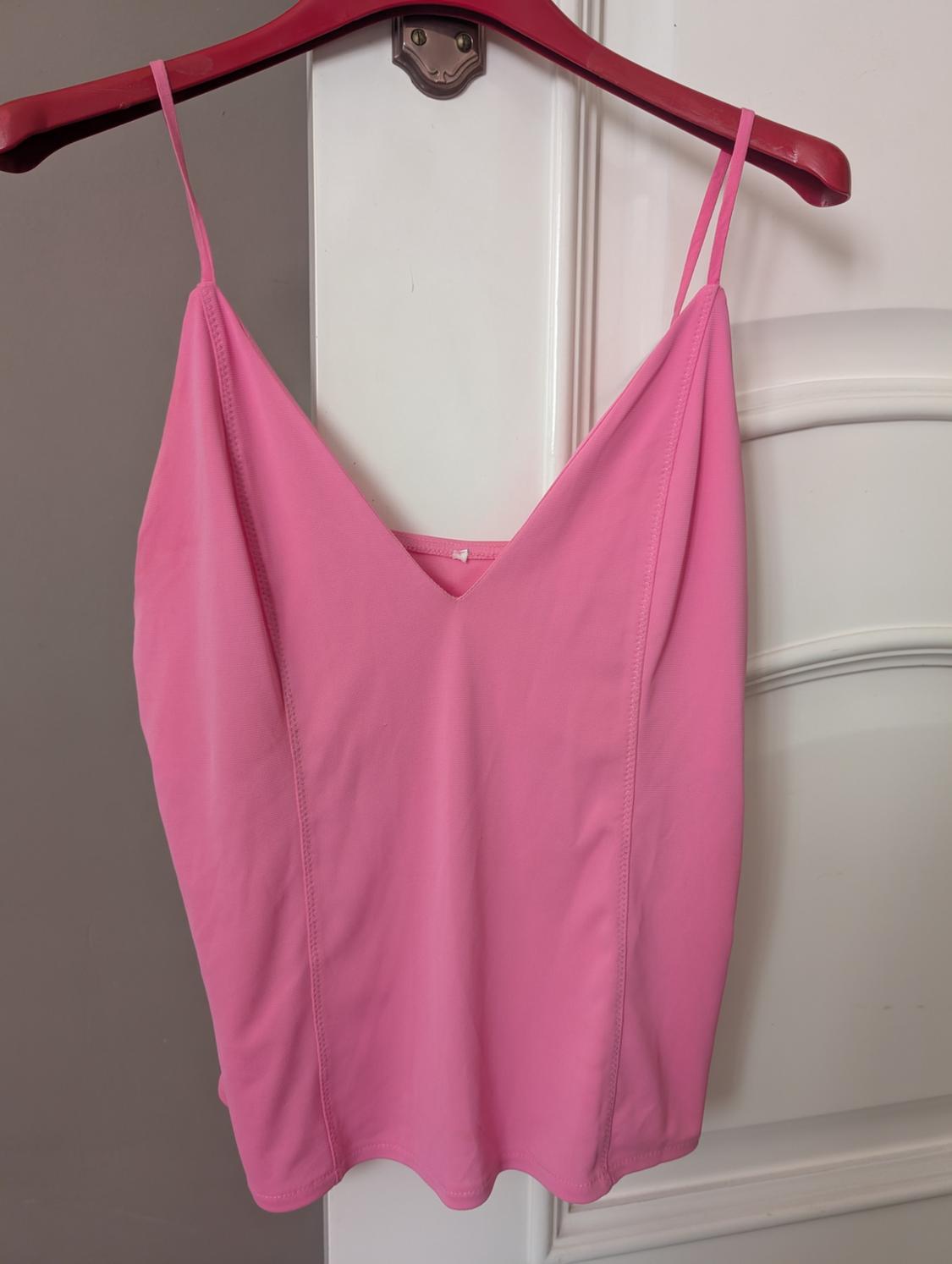 Pink camisole top hanging on a red hanger over a white door.