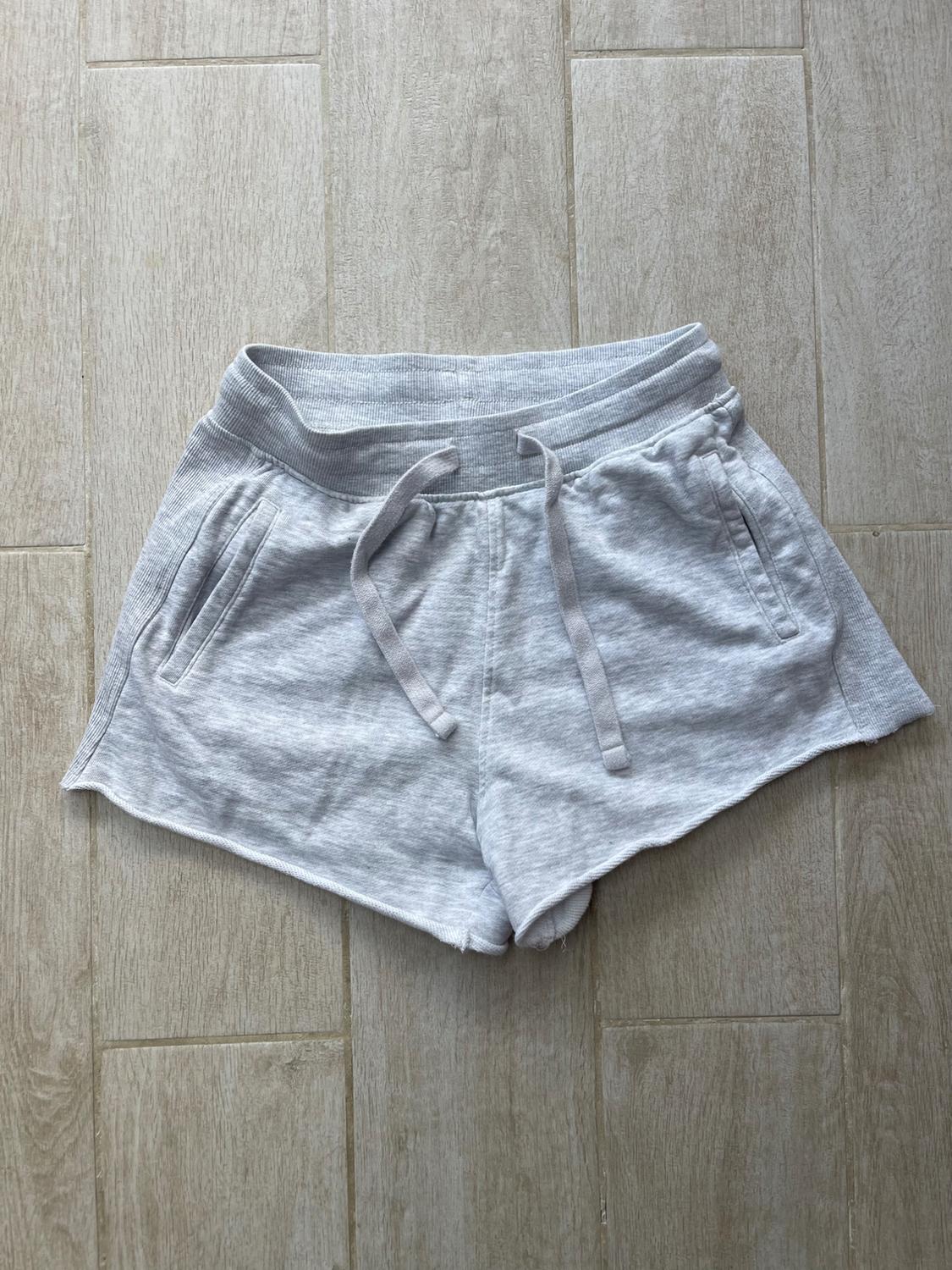 Grey soft-touch shorts with elasticated waistband and adjustable drawstrings, side pockets, on a light wood background.