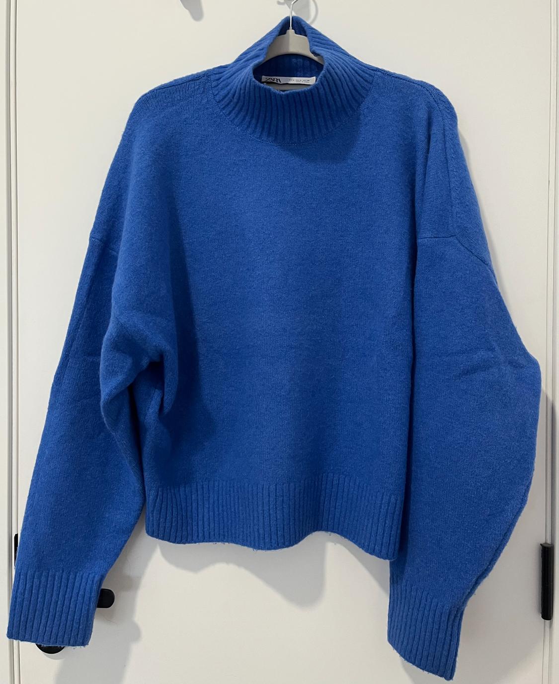 Blue roll-neck jumper hanging on a hanger over a white door.