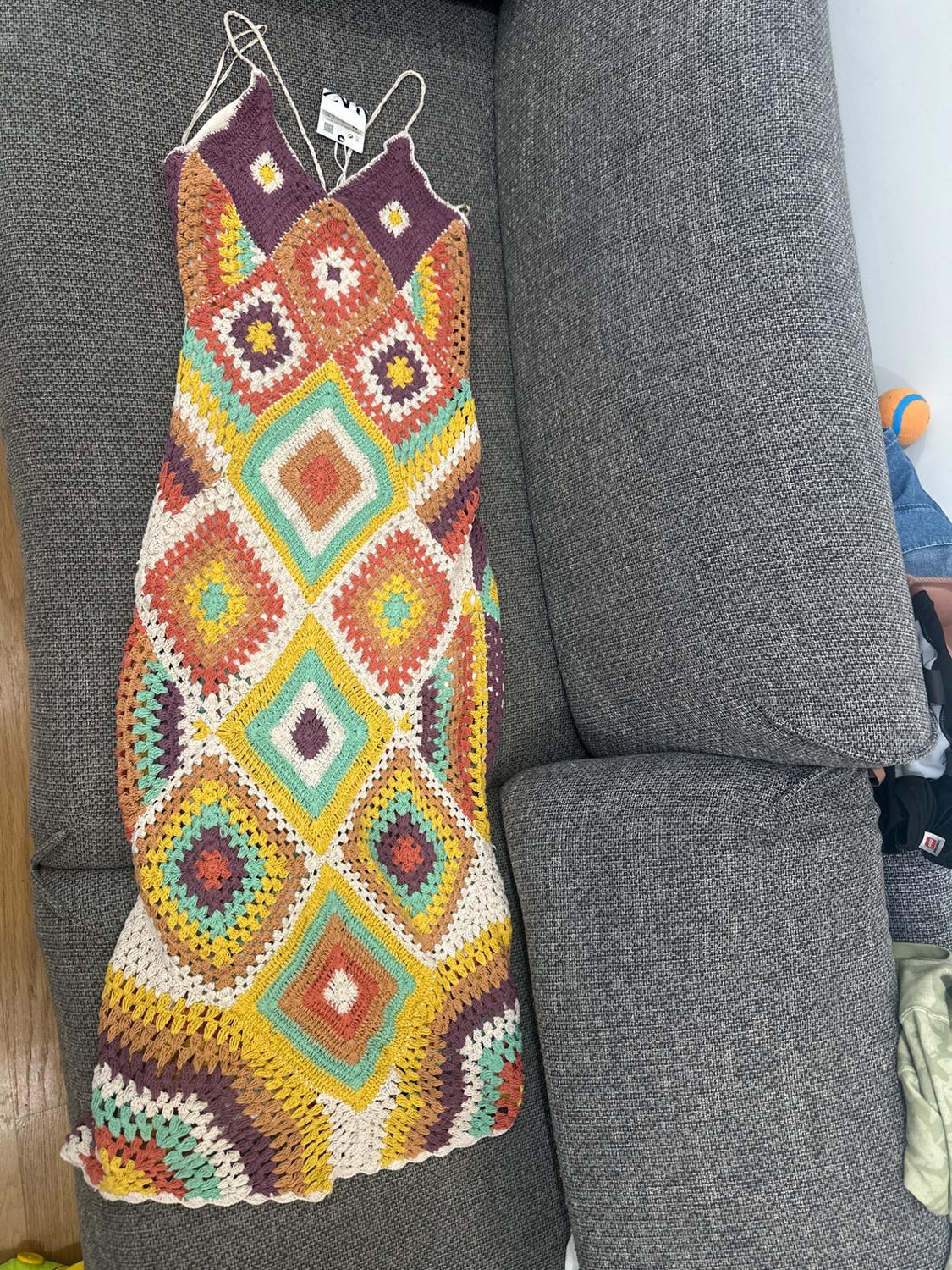 Multicolor crochet dress with geometric patterns on a gray sofa. Label visible on the top of the dress.