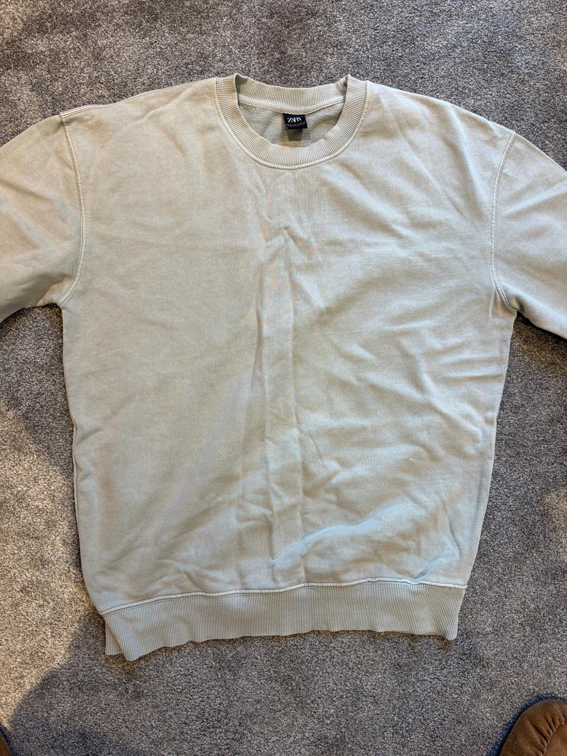 Long-sleeved, round-neck sweatshirt in greyish light green with ZARA label, on a grey rug.